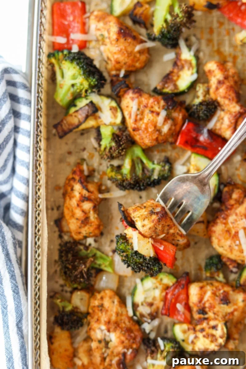 Crispy Air Fryer Chicken and Veggies 12 A fork lifts a perfectly cooked piece of chicken, a vibrant red bell pepper, and a broccoli floret from the air fryer tray, ready to be enjoyed.