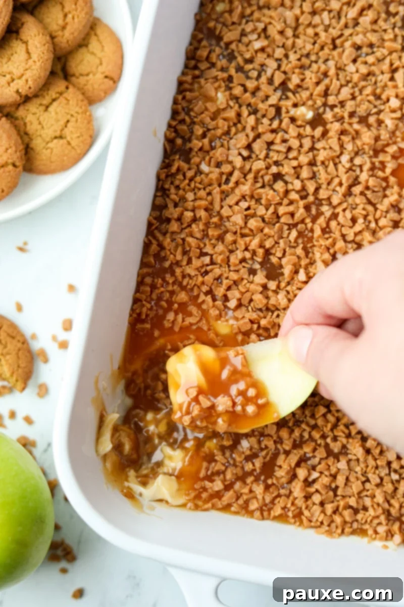 Irresistible Caramel Apple Delight 2 Dipping a crisp green apple slice into a rich, creamy caramel dip, generously topped with glistening toffee bits, ready for a delicious bite.