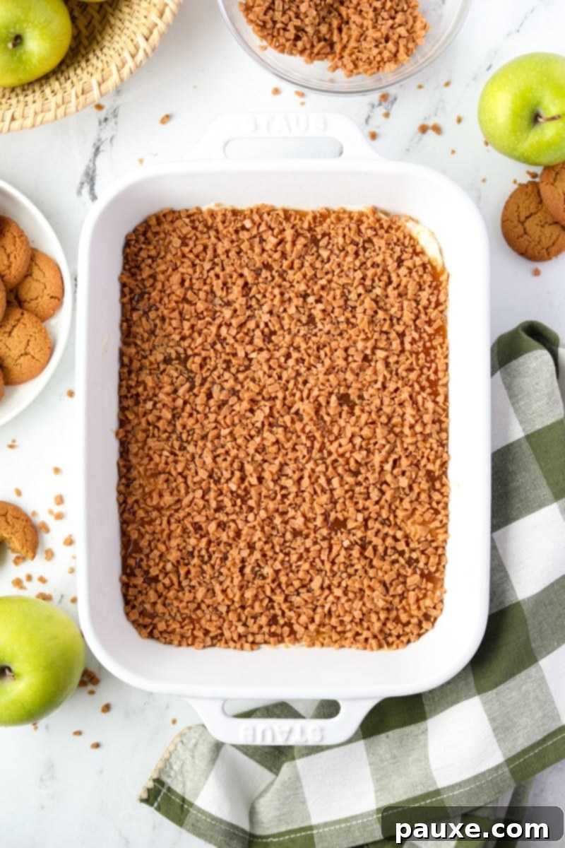Irresistible Caramel Apple Delight 11 A close-up of a baking dish filled with a smooth cream cheese layer, beautifully sprinkled with crunchy toffee bits, awaiting the caramel.