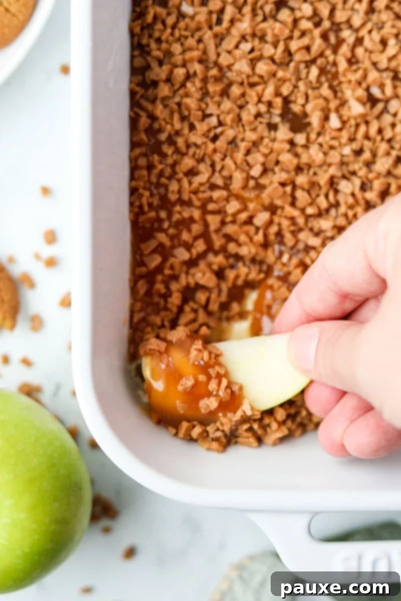 Irresistible Caramel Apple Delight 12 A hand gently dipping a crisp slice of Granny Smith apple into the luxurious caramel and cream cheese dip, beautifully showcasing the perfect coating and inviting texture.