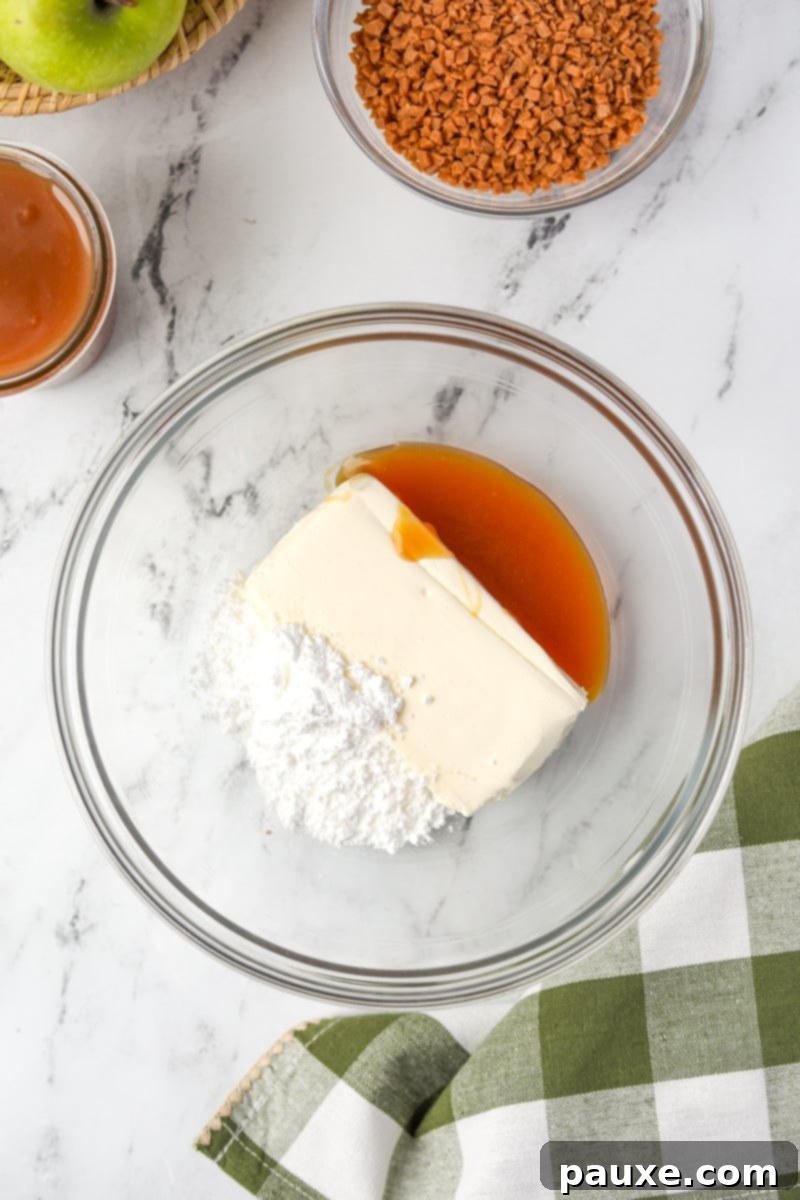 Irresistible Caramel Apple Delight 4 A mixing bowl containing softened cream cheese, powdered sugar, and a initial portion of caramel sauce, perfectly ready for blending.