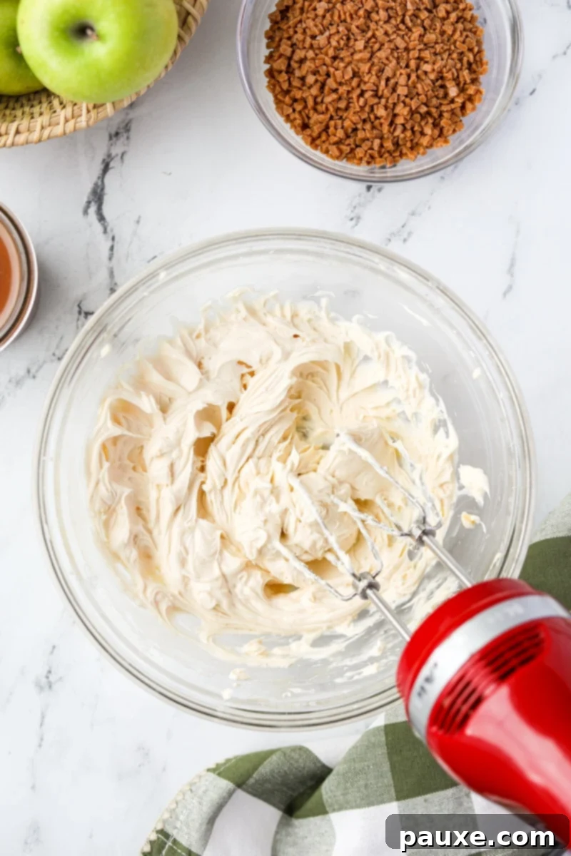 Irresistible Caramel Apple Delight 5 An electric hand mixer actively blending the cream cheese, caramel, and sugar mixture in a large bowl until it becomes smooth and homogenous.