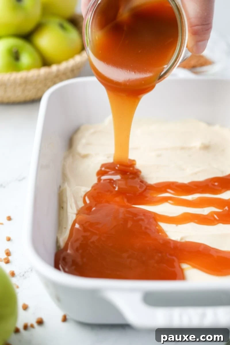 Irresistible Caramel Apple Delight 7 Thick, golden caramel sauce being artfully drizzled in a spiral pattern over the smooth white cream cheese layer in a baking dish.