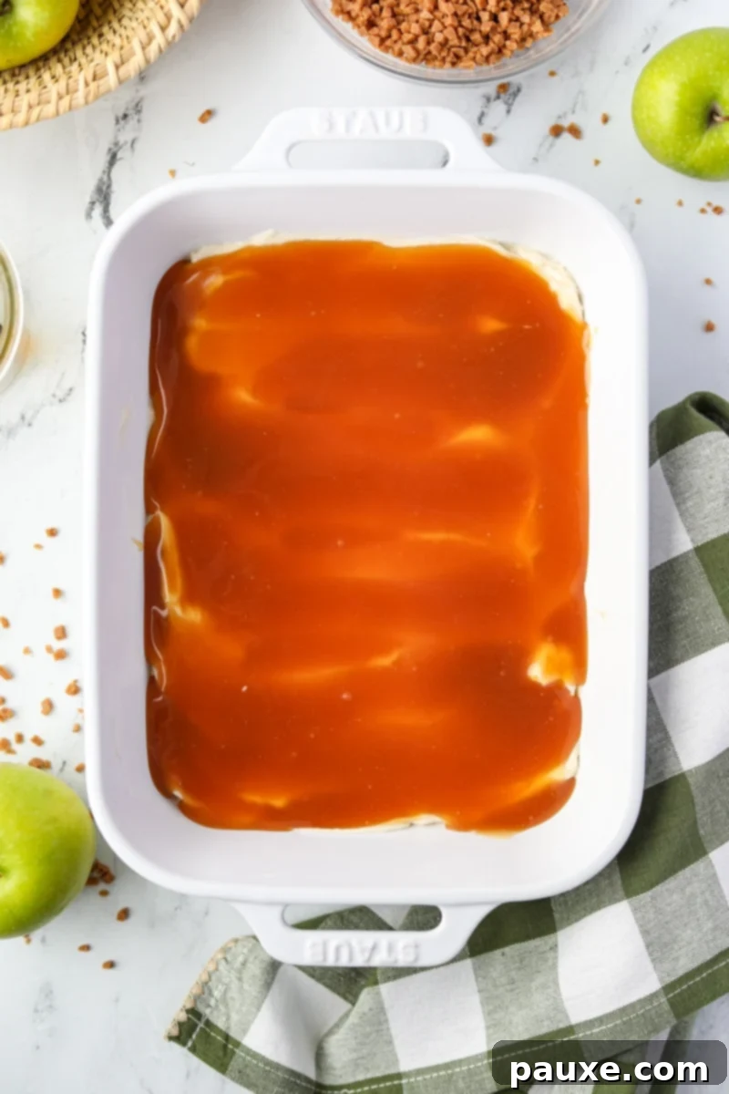 Irresistible Caramel Apple Delight 8 A close-up view of rich, golden caramel sauce being carefully smoothed over a pristine layer of cream cheese using a silicone spatula.