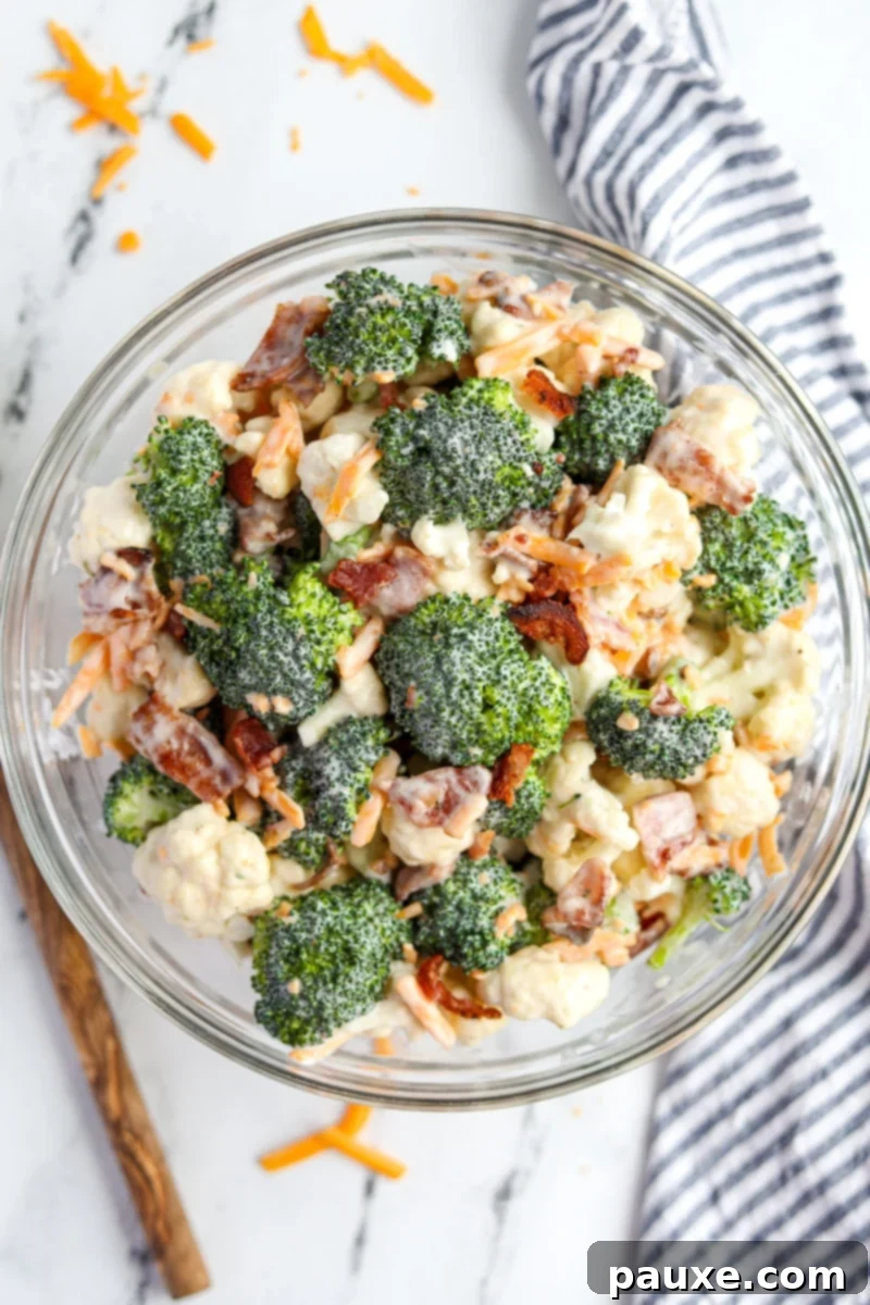 Creamy Amish Broccoli Salad 2 A large bowl of vibrant Amish broccoli salad, featuring green broccoli florets, white cauliflower, golden shredded cheddar cheese, and crispy bacon bits, ready to be served.