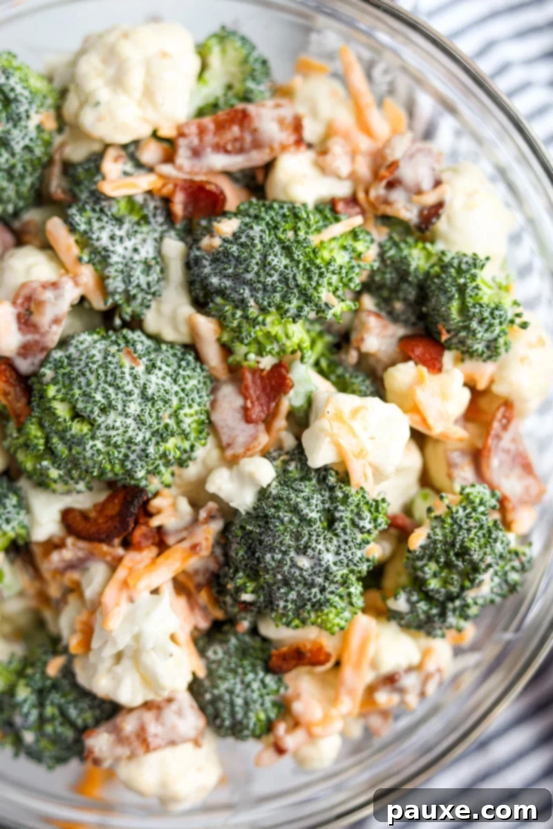 Creamy Amish Broccoli Salad 12 A close-up, appetizing view of a bowl of creamy Amish broccoli salad, showcasing the detailed textures of raw broccoli and cauliflower florets, rich shredded cheddar cheese, and crunchy bacon pieces, all coated in the signature sweet dressing.