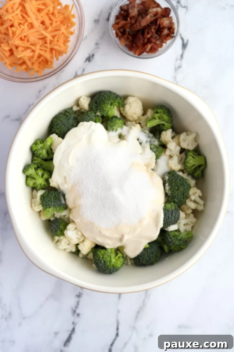 Creamy Amish Broccoli Salad 5 A creamy white dressing, made from mayonnaise, sour cream, sugar, and salt, artfully dolloped over a mound of raw broccoli and cauliflower florets in a large bowl, ready to be mixed.