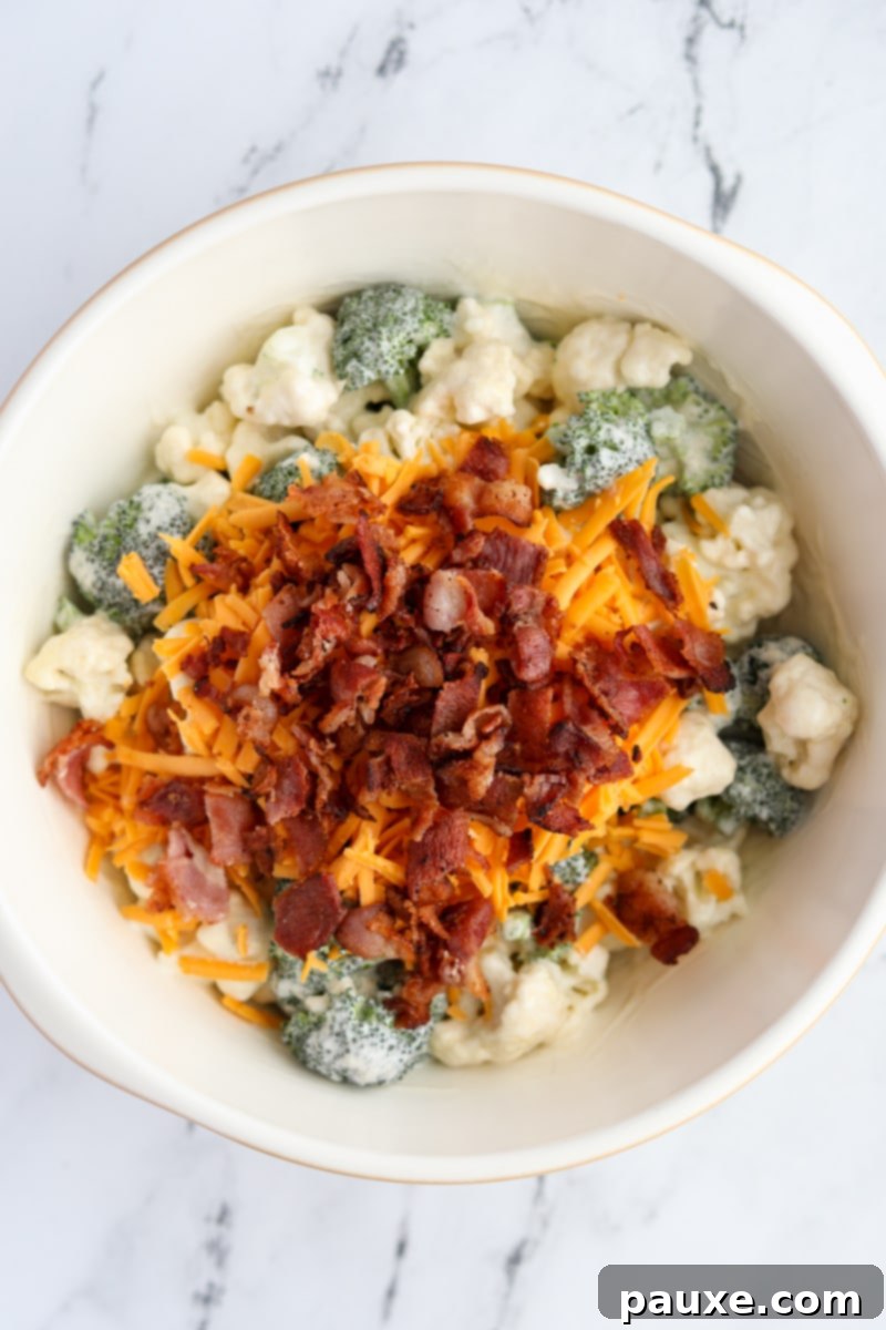 Creamy Amish Broccoli Salad 7 A large bowl containing dressed broccoli and cauliflower florets, topped with a generous layer of freshly shredded sharp cheddar cheese and perfectly crispy, crumbled bacon pieces.