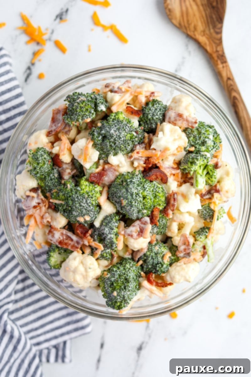 Creamy Amish Broccoli Salad 8 A beautifully mixed bowl of Amish broccoli salad, showcasing a delightful blend of creamy dressed broccoli and cauliflower florets, interspersed with vibrant shredded cheddar cheese and savory crumbled bacon, ready to serve.