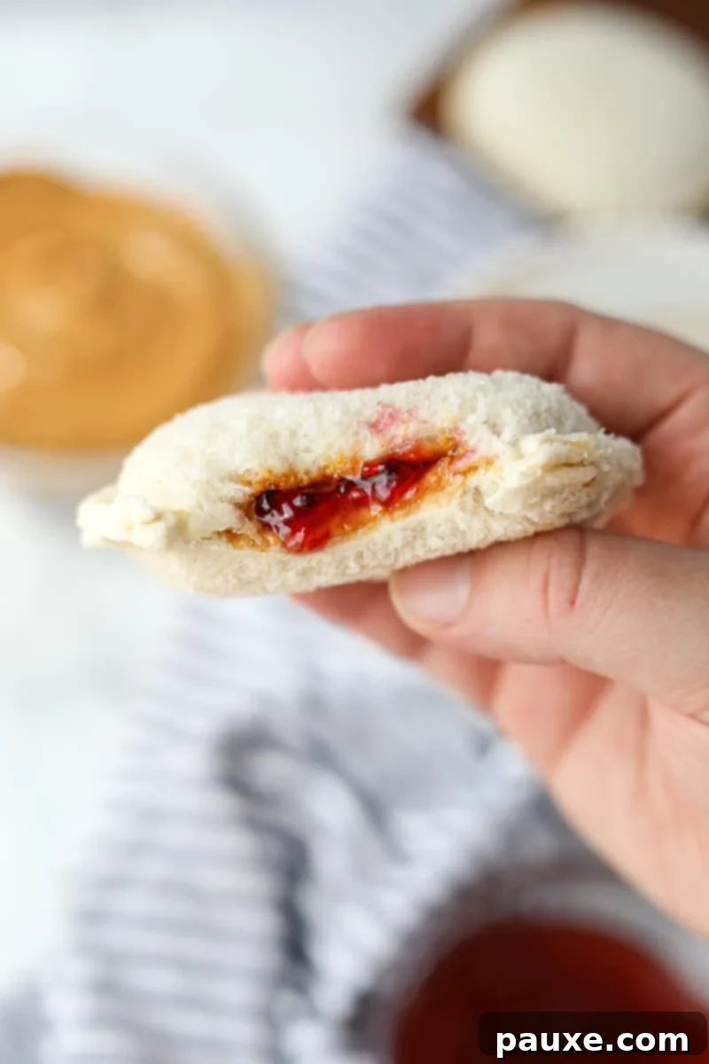 DIY Crustless Sandwich Pockets 2 A hand holding a perfectly round, sealed peanut butter and jelly sandwich, showcasing the classic crustless design of a homemade uncrustable.