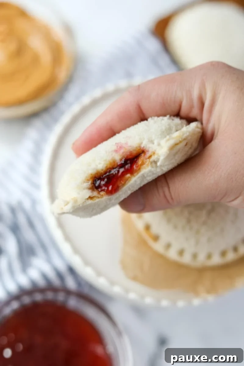 DIY Crustless Sandwich Pockets 12 A hand gently squeezing a sealed, round homemade peanut butter and jelly sandwich, demonstrating its soft and pliable texture after thawing.