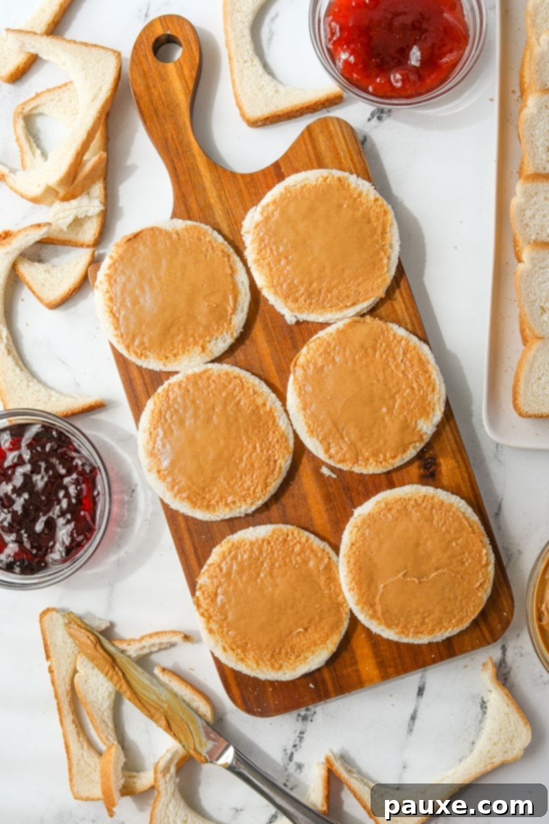 DIY Crustless Sandwich Pockets 6 A hand smoothly spreading creamy peanut butter onto a circular piece of bread, leaving a small margin around the edge.