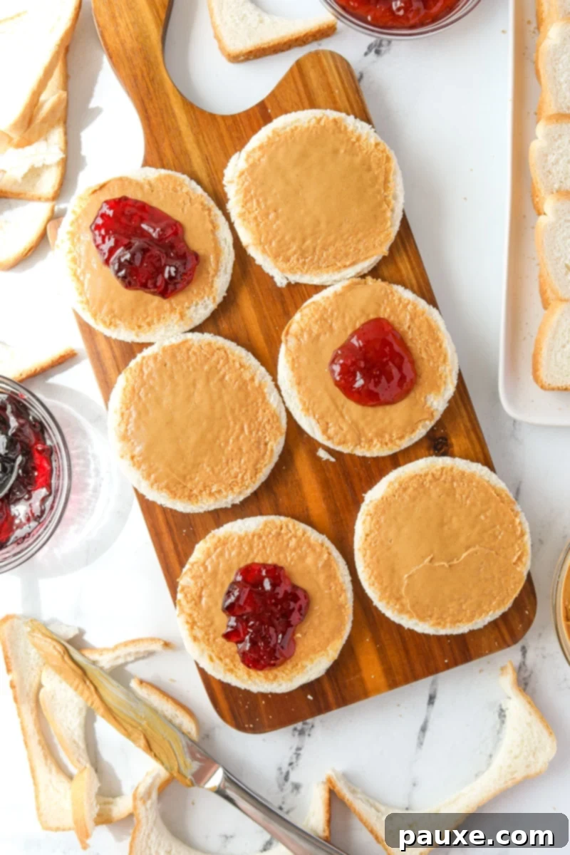 DIY Crustless Sandwich Pockets 7 A spoonful of vibrant jelly being carefully placed on top of a peanut butter-coated bread round, maintaining the clear edge.