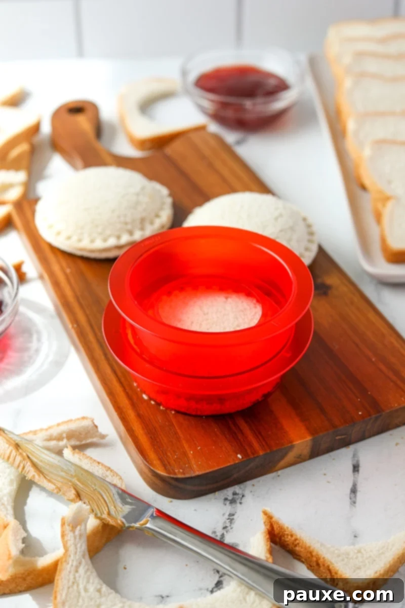 DIY Crustless Sandwich Pockets 9 A sandwich sealer firmly pressing two peanut butter and jelly-filled bread rounds together, crimping and sealing the edges to create a crustless sandwich.