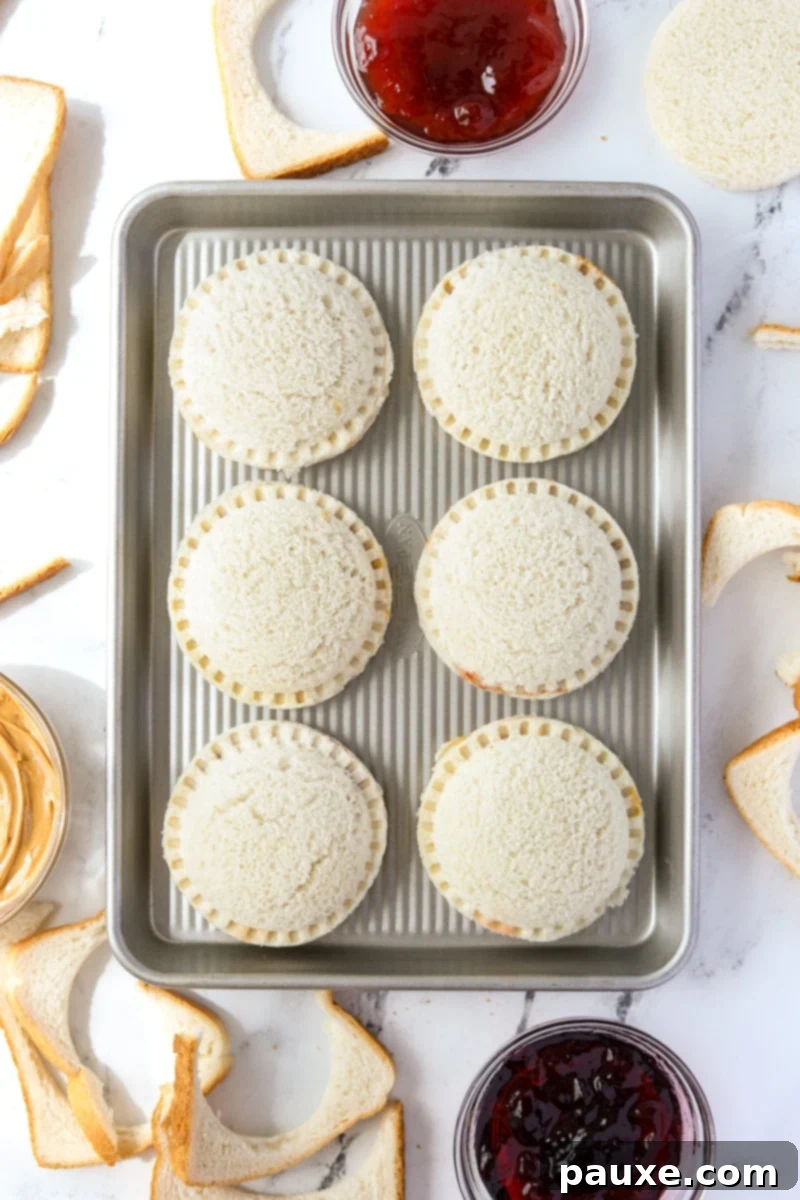 DIY Crustless Sandwich Pockets 10 A baking sheet lined with parchment paper, neatly holding several round, sealed peanut butter and jelly sandwiches, ready for flash freezing.