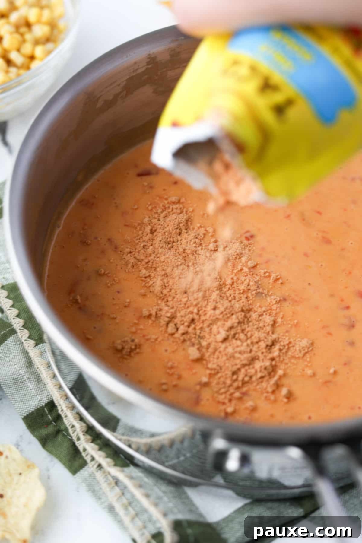 Zesty Fiesta Dip 6 Taco seasoning being sprinkled over the melted Rotel and Velveeta dip in a saucepan.