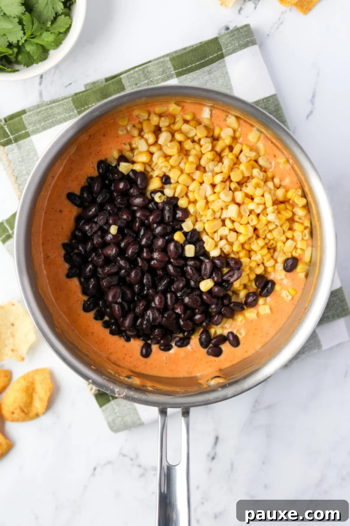 Zesty Fiesta Dip 8 Canned black beans and corn being added to the melted Rotel dip in a saucepan.