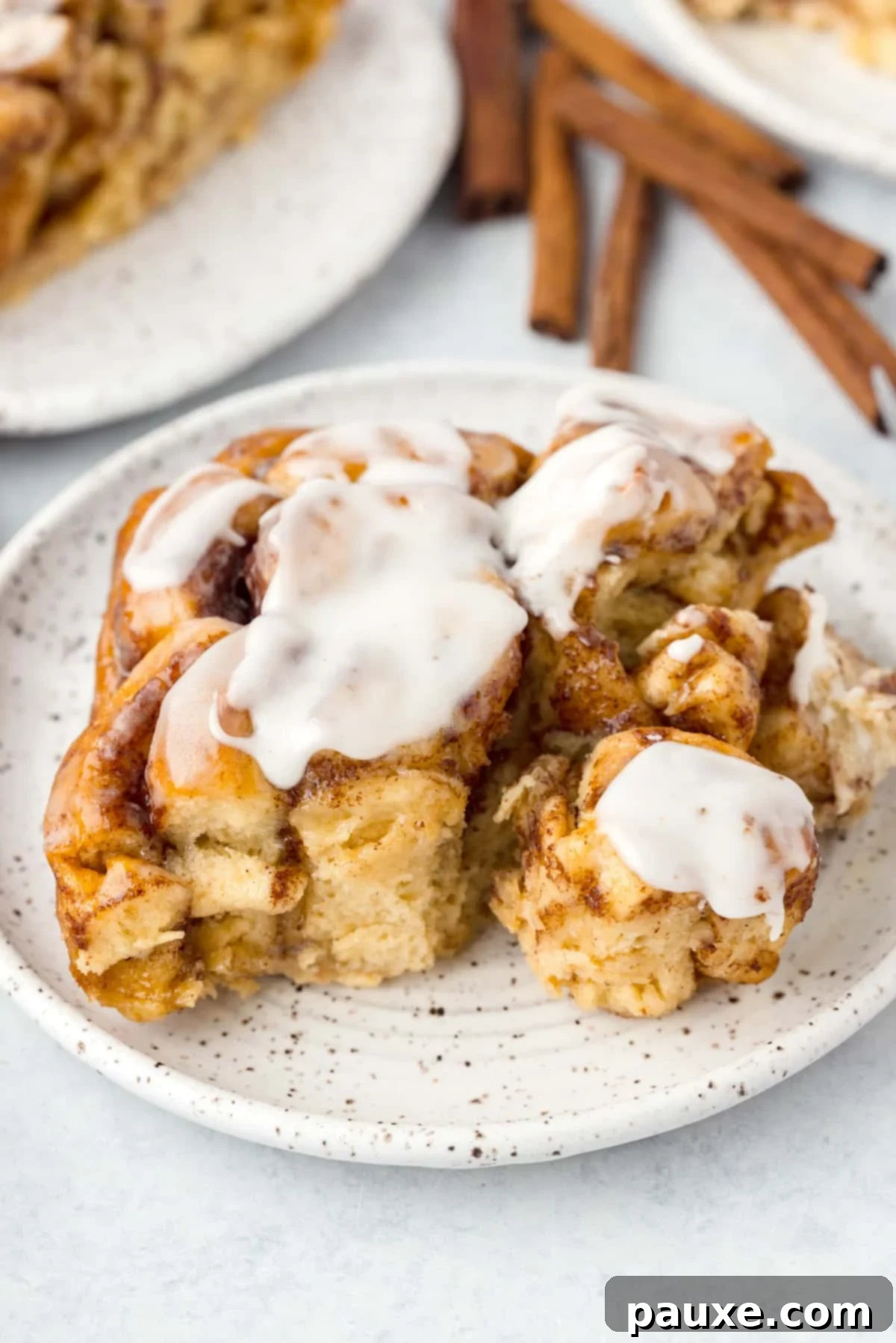 Gooey Cinnamon Bliss Bake 2 A slice of warm cinnamon roll casserole on a white plate, topped with a generous drizzle of white icing.