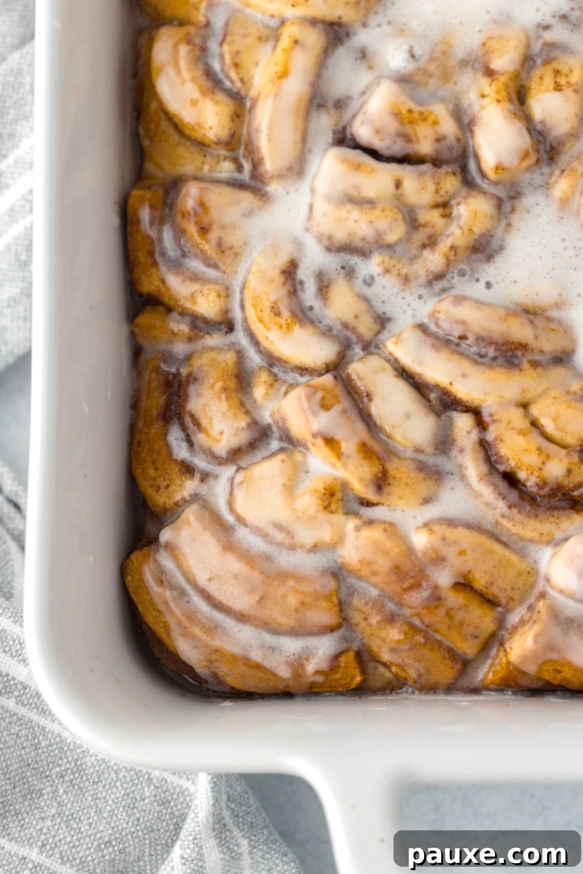 Gooey Cinnamon Bliss Bake 14 A large baking dish showcasing the golden-brown baked cinnamon roll casserole, generously covered with sweet white icing.