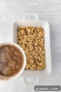 Gooey Cinnamon Bliss Bake 19 Pouring a custard mixture over a baking dish filled with cinnamon roll pieces.