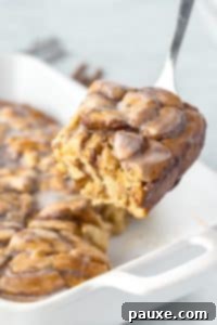 Gooey Cinnamon Bliss Bake 21 Lifting a portion of cinnamon roll breakfast bake from a baking dish.