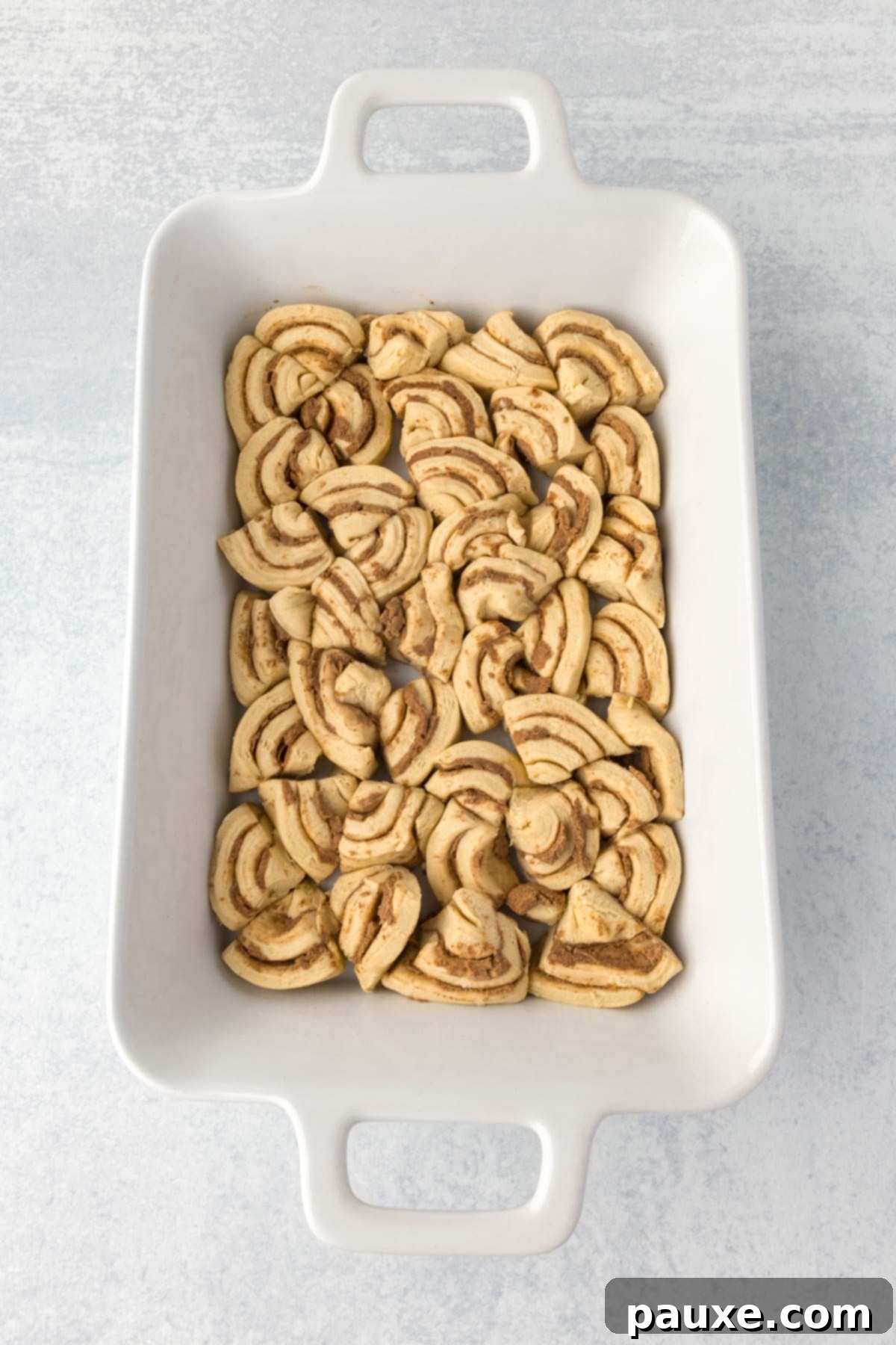 Gooey Cinnamon Bliss Bake 5 Quartered cinnamon roll pieces arranged in a single, even layer within a greased baking dish.
