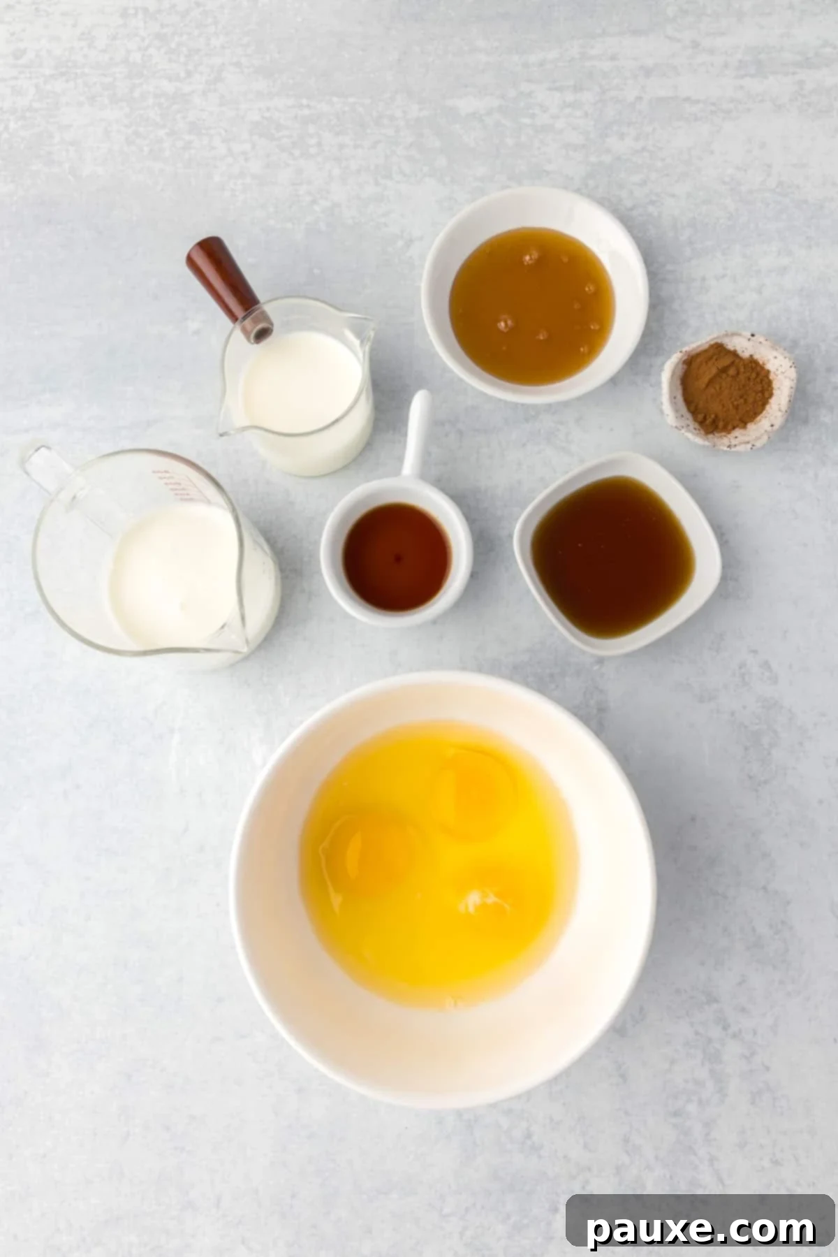 Gooey Cinnamon Bliss Bake 6 A bowl filled with whisked eggs, surrounded by small containers of milk, buttermilk, honey, maple syrup, vanilla, and cinnamon.