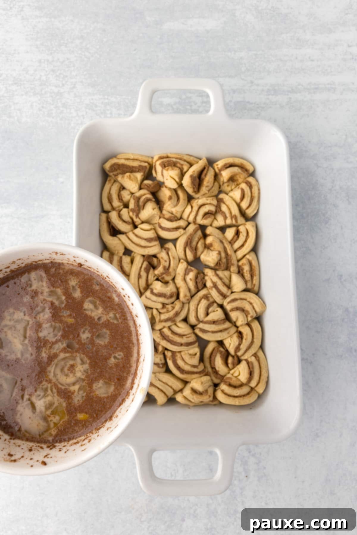 Gooey Cinnamon Bliss Bake 8 Pouring the creamy custard mixture evenly over the scattered cinnamon roll pieces in the baking dish.