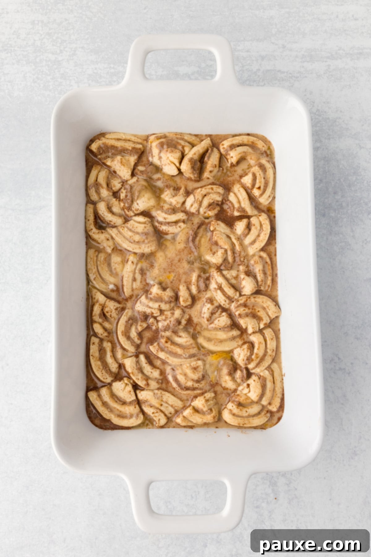 Gooey Cinnamon Bliss Bake 9 A baking dish filled with quartered cinnamon rolls soaked in the custard mixture, ready for baking.