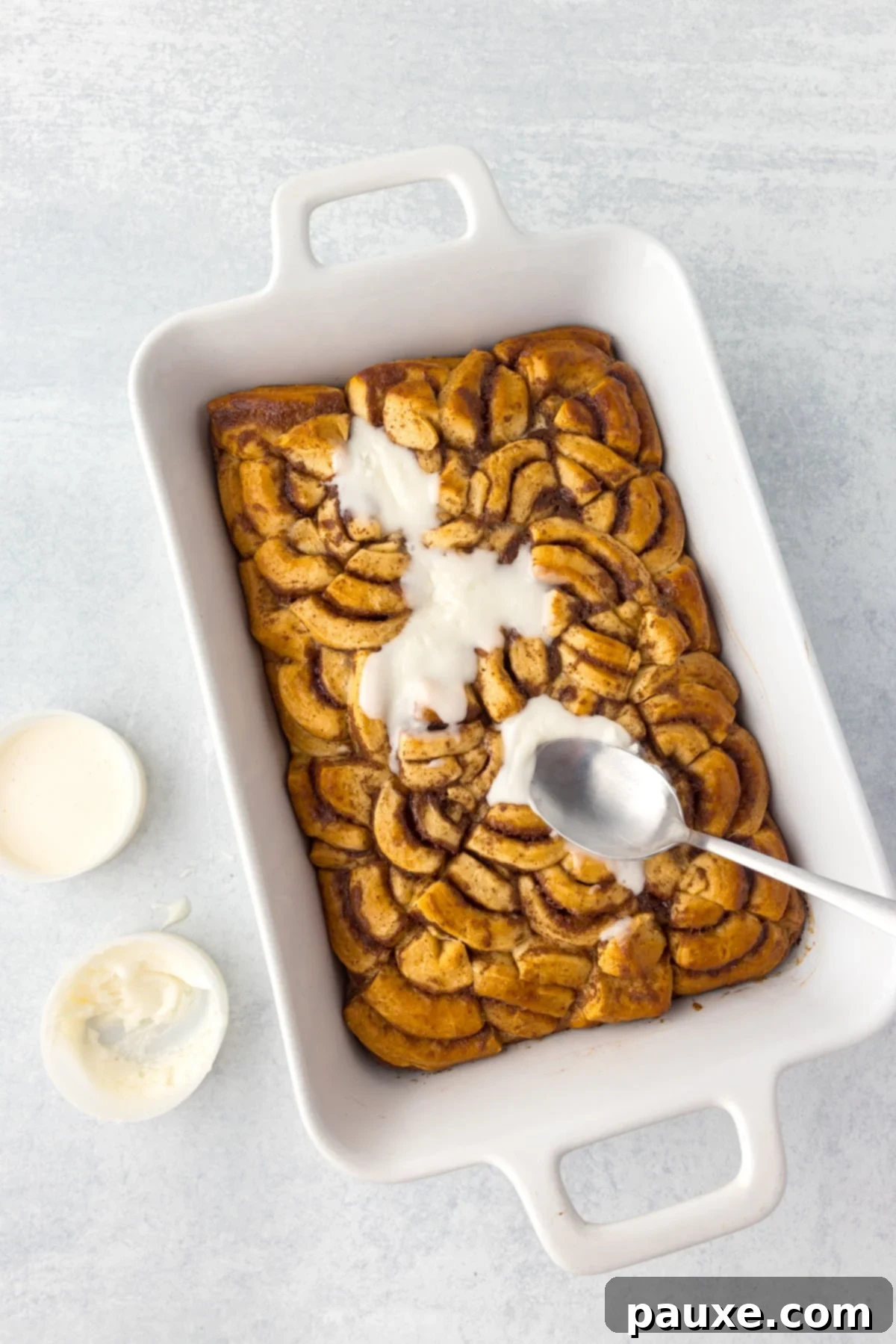 Gooey Cinnamon Bliss Bake 10 Spreading the sweet white icing over the top of the freshly baked and warm cinnamon roll casserole.