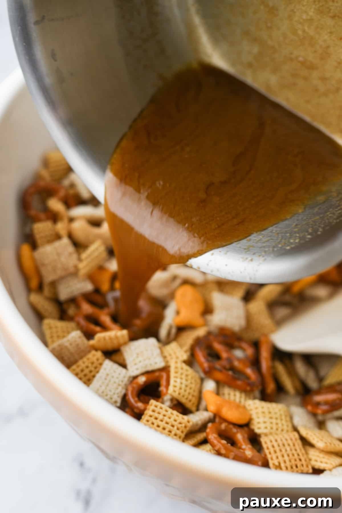 Savory Goldfish Crunch Mix 7 Pouring butter and seasonings over a dry snack mix in a large bowl.