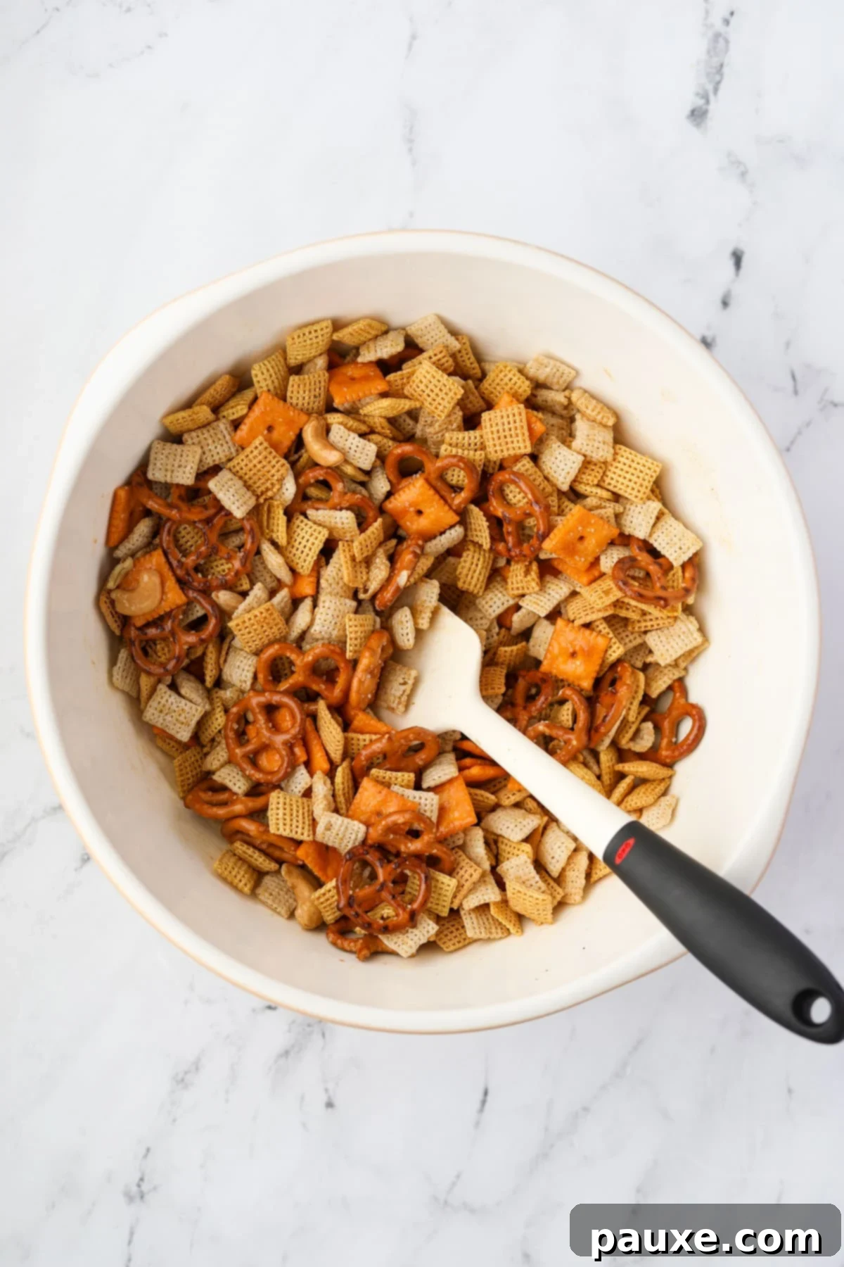 Savory Snack Medley 7 A bowl of Chex Mix being thoroughly stirred with a silicone spatula to coat all ingredients evenly.