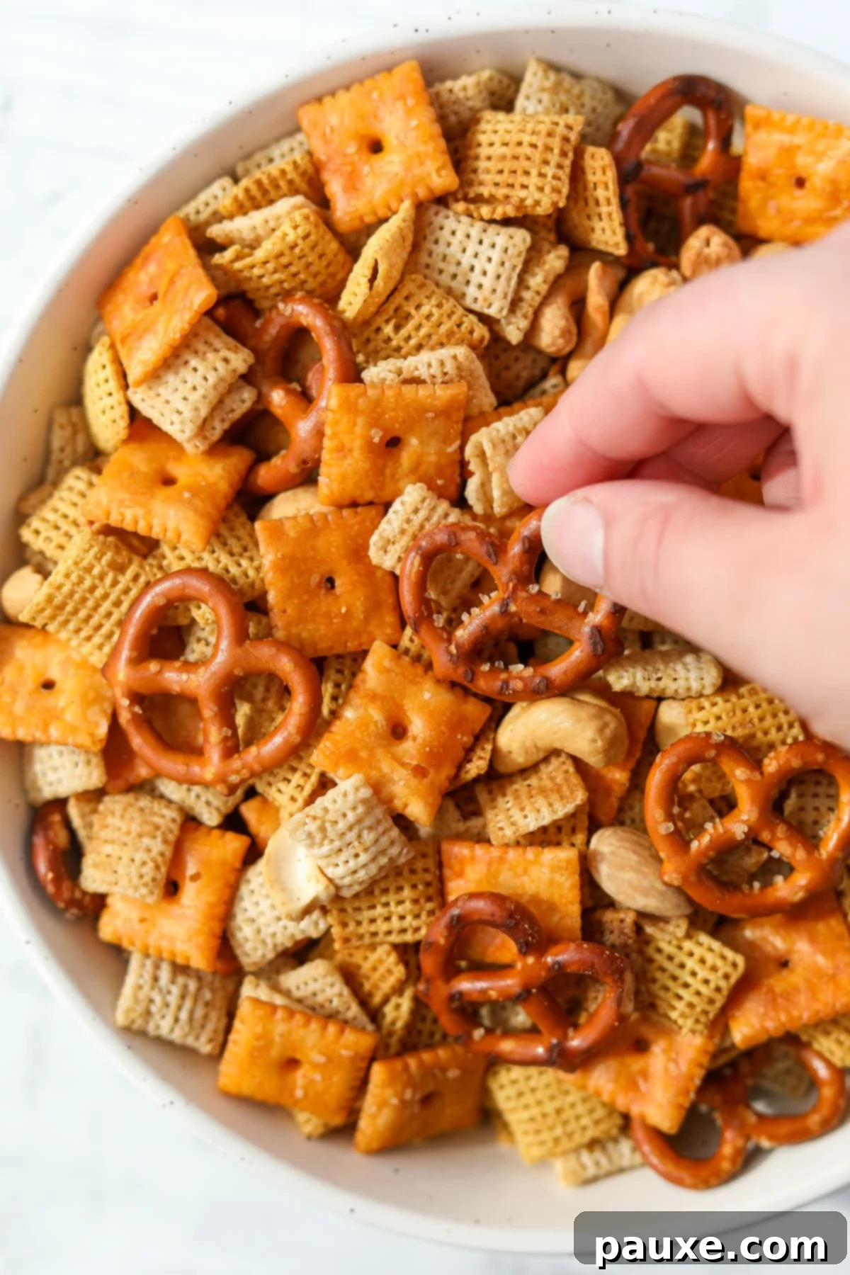 Savory Snack Medley 10 A hand reaching into a bowl of perfectly baked Chex Mix to grab a pretzel, highlighting its irresistible appeal.