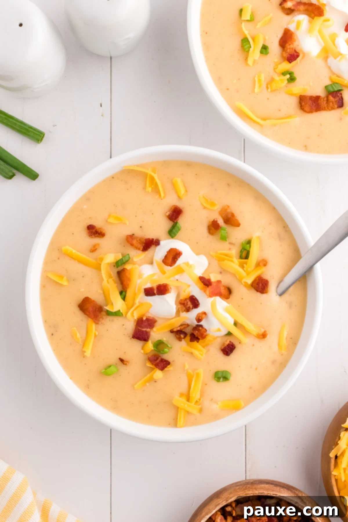 A steaming bowl of creamy Loaded Baked Potato Soup garnished with crispy bacon, shredded cheese, and green onions.