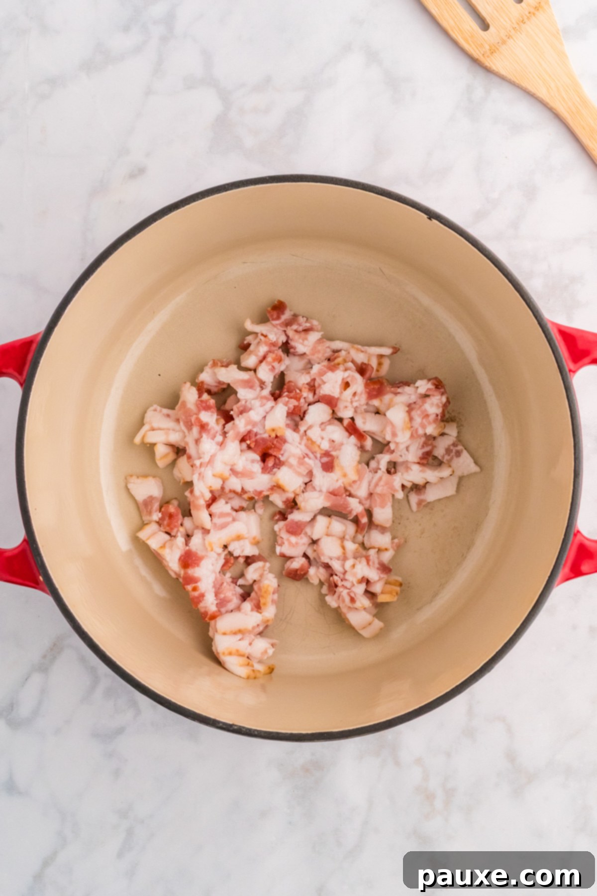 Raw bacon pieces cooking in a Dutch oven, rendering fat.