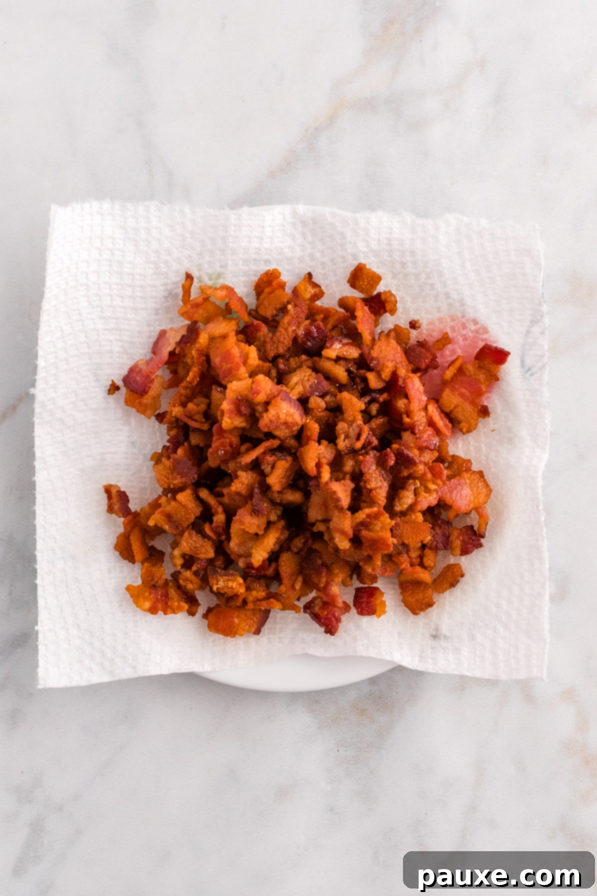 Crispy cooked bacon bits draining on a paper towel-lined plate.