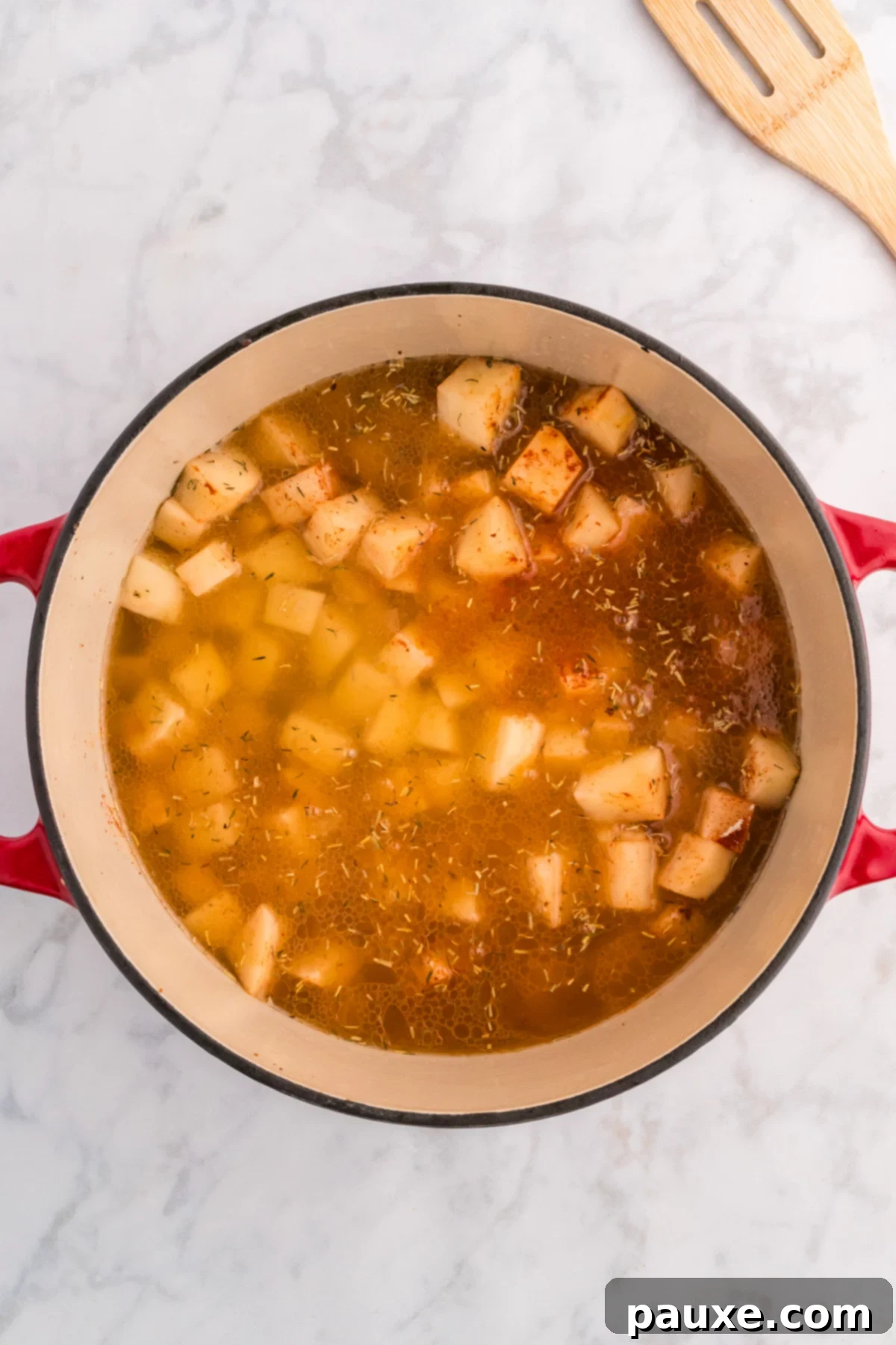 Chicken broth being poured over potatoes and onions in a Dutch oven.