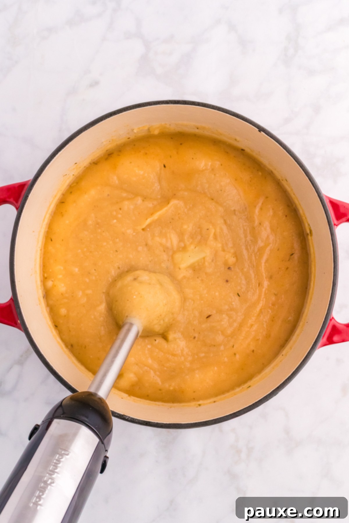An immersion blender pureeing potato soup in a Dutch oven, leaving some chunks for texture.