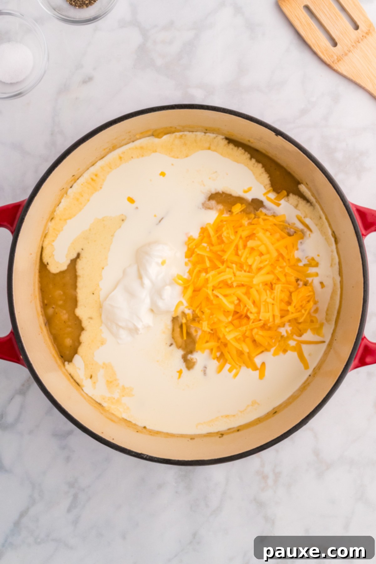 Heavy cream, sour cream, and shredded cheddar cheese being added to partially blended potato soup.