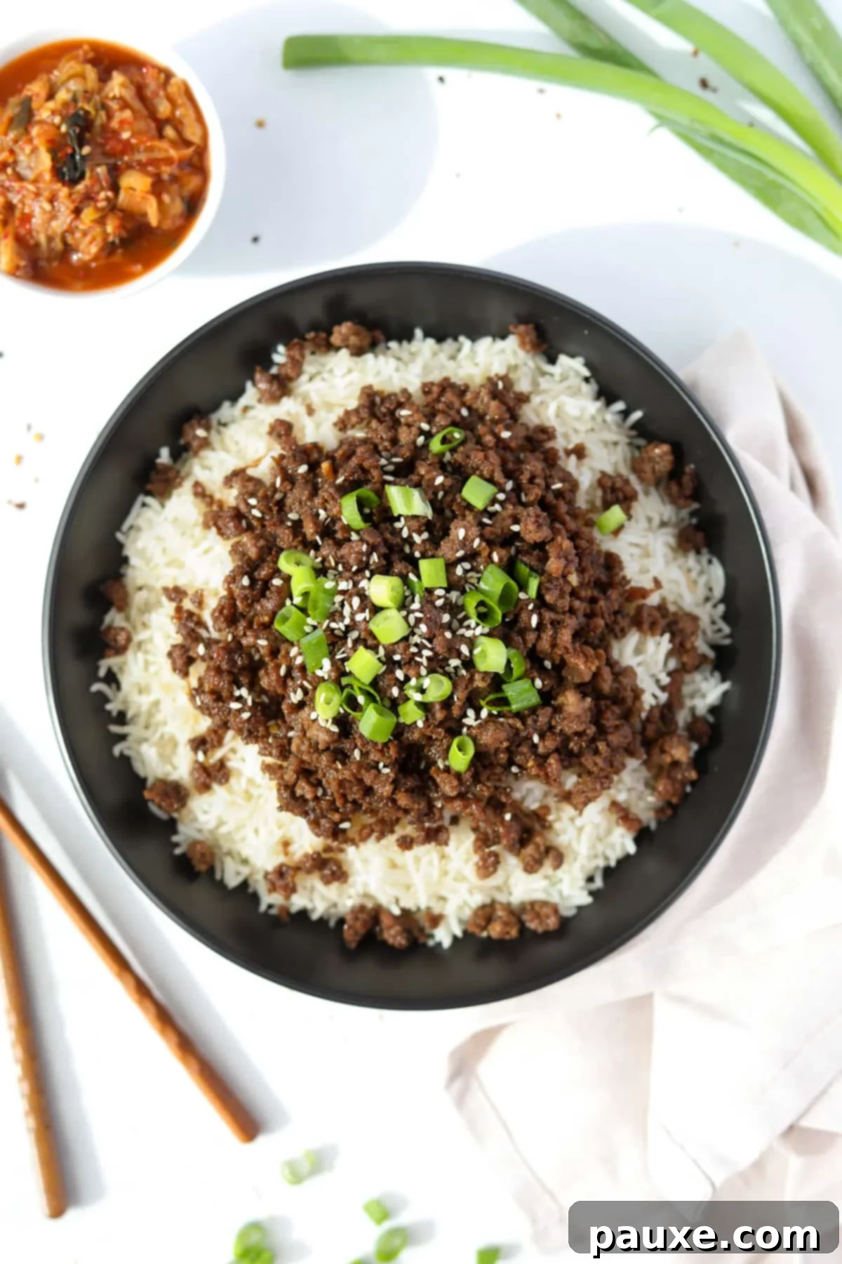 Authentic Korean Marinated Beef 8 A bowl filled with steaming white rice and generously topped with seasoned ground beef, vibrant green onions, and crunchy sesame seeds.