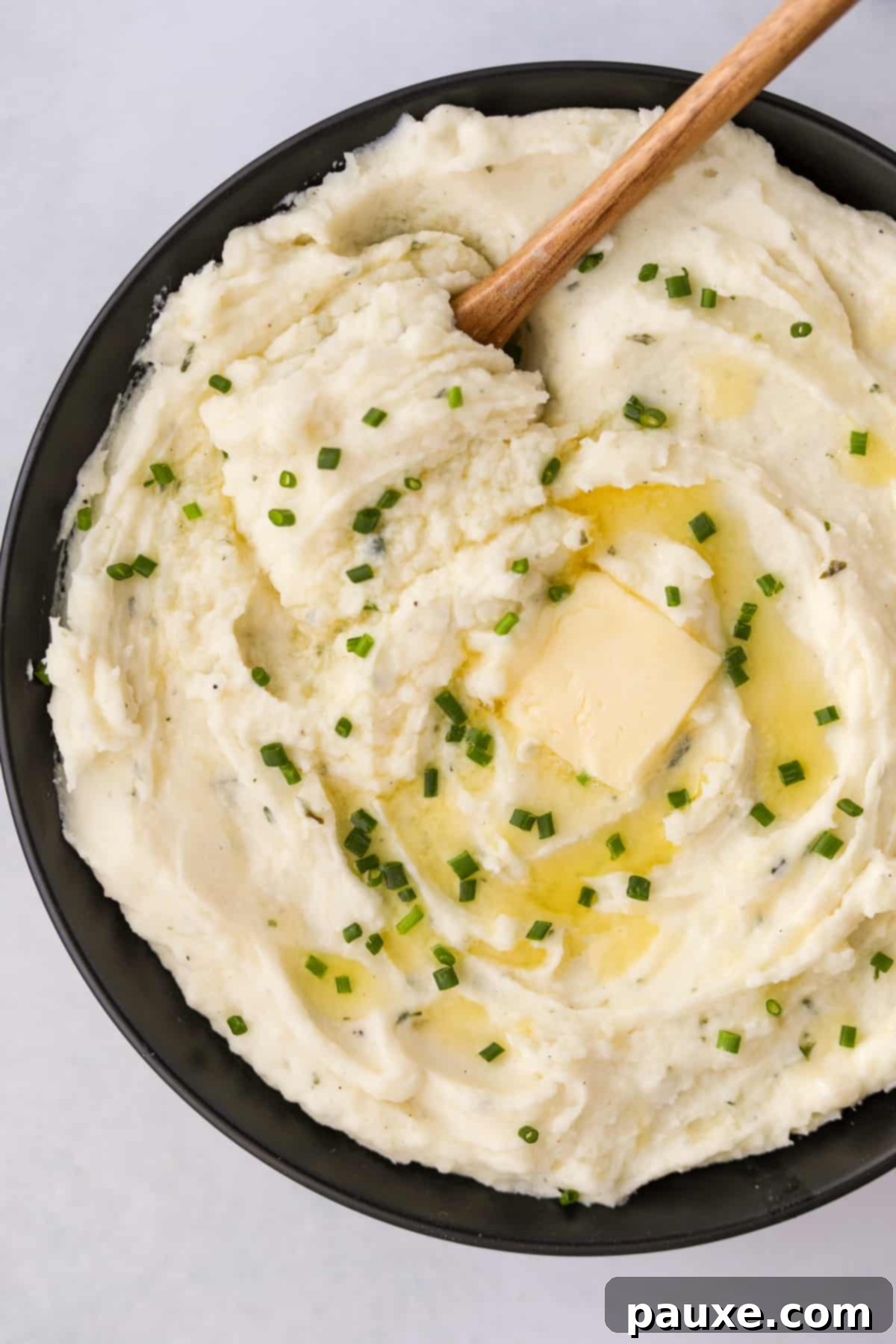 Creamy Garlic Herb Boursin Mash 2 A black bowl filled with mashed potatoes and topped with melted butter and chives.