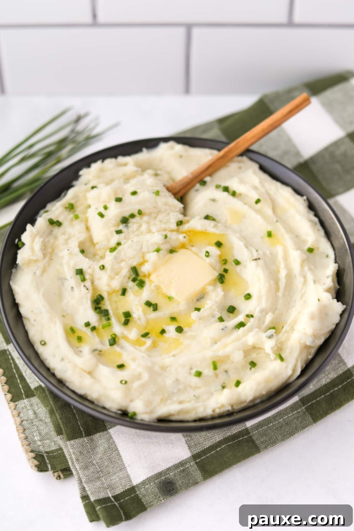 Creamy Garlic Herb Boursin Mash 11 A large bowl filled with mashed potaotes and topped with a pat of butter and some fresh chives.