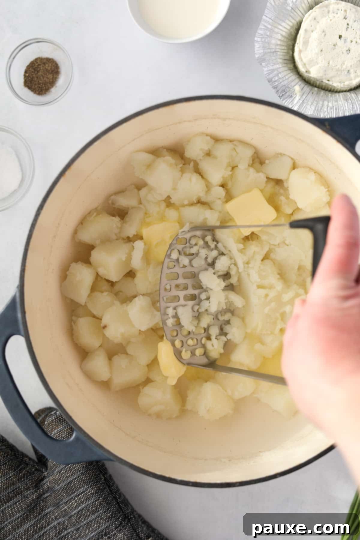 Creamy Garlic Herb Boursin Mash 6 Using a potato masher to mash potatoes in a Dutch Oven.