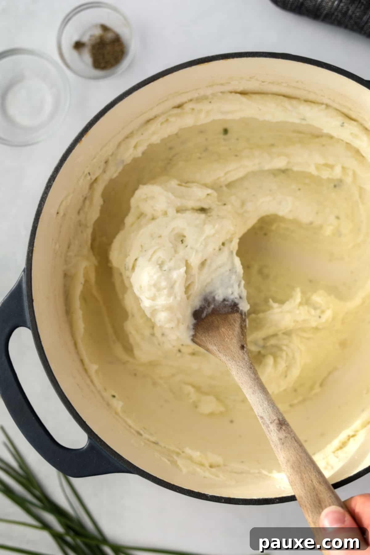 Creamy Garlic Herb Boursin Mash 9 A wooden spoon whipping potatoes in a Dutch Oven.