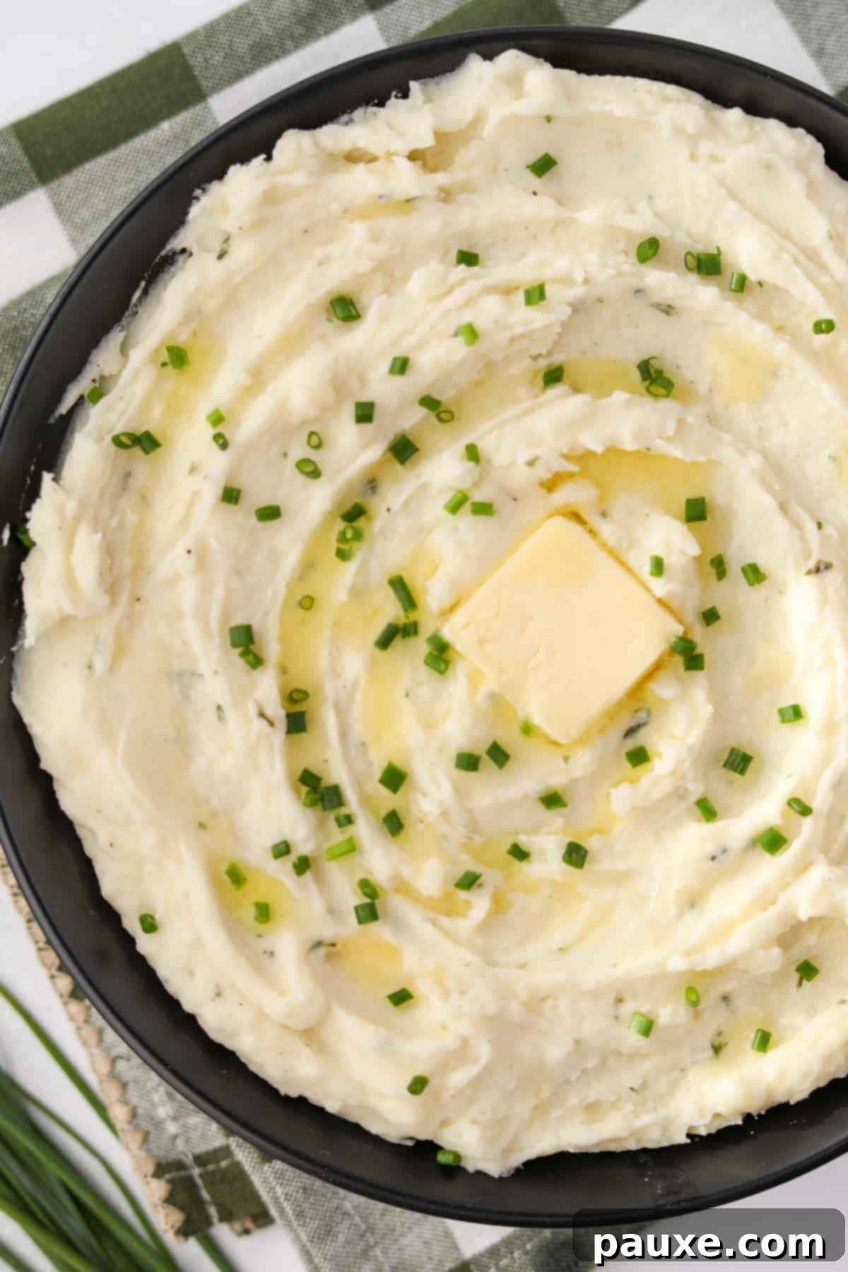 Creamy Garlic Herb Boursin Mash 10 A black bowl filled with creamy mashed potatoes, topped with butter and chives.