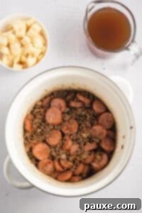 Rancher's Hearty Stew 19 Ground beef and sliced sausages with seasonings in a soup pot.