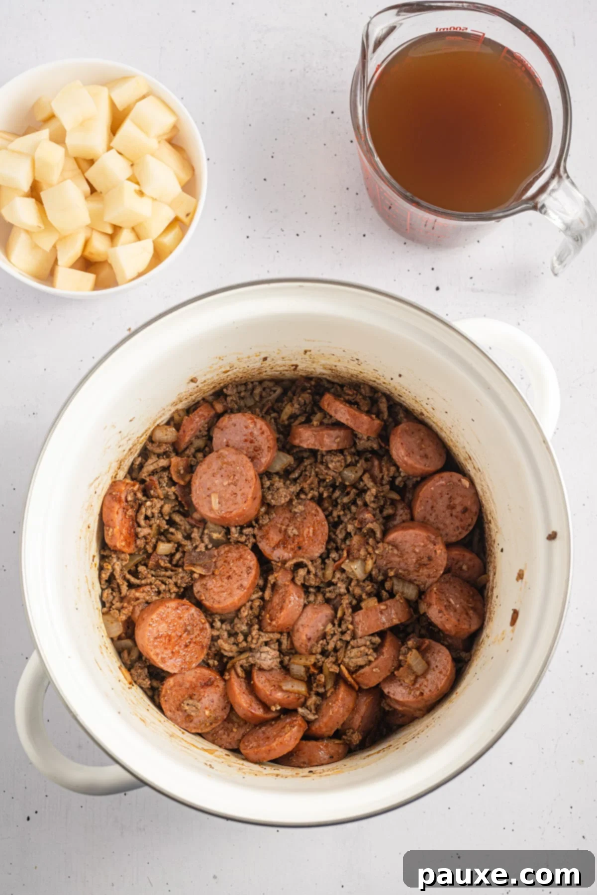 Rancher's Hearty Stew 6 A soup pot containing browned ground beef and sliced smoked sausage, along with crispy bacon bits, all seasoned and ready for the liquid ingredients.
