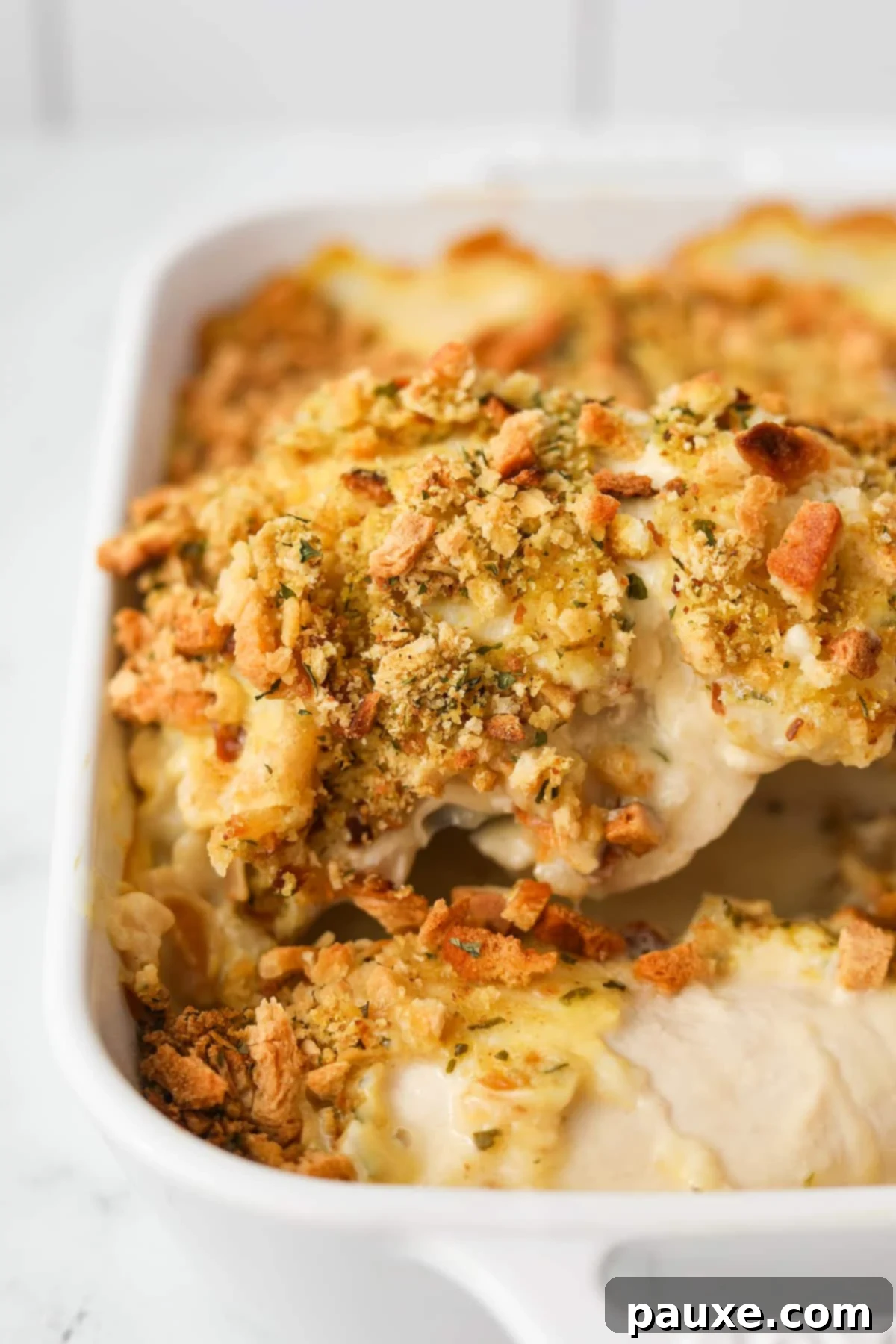 Alpine Chicken Comfort Bake 2 Lifting a chicken breast topped with stuffing mix from a baking dish, showcasing the golden-brown crust and creamy interior.