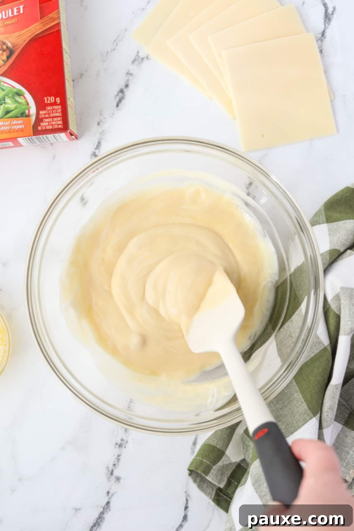 Alpine Chicken Comfort Bake 5 Someone stirring together cream of chicken soup and sour cream in a bowl until smooth.