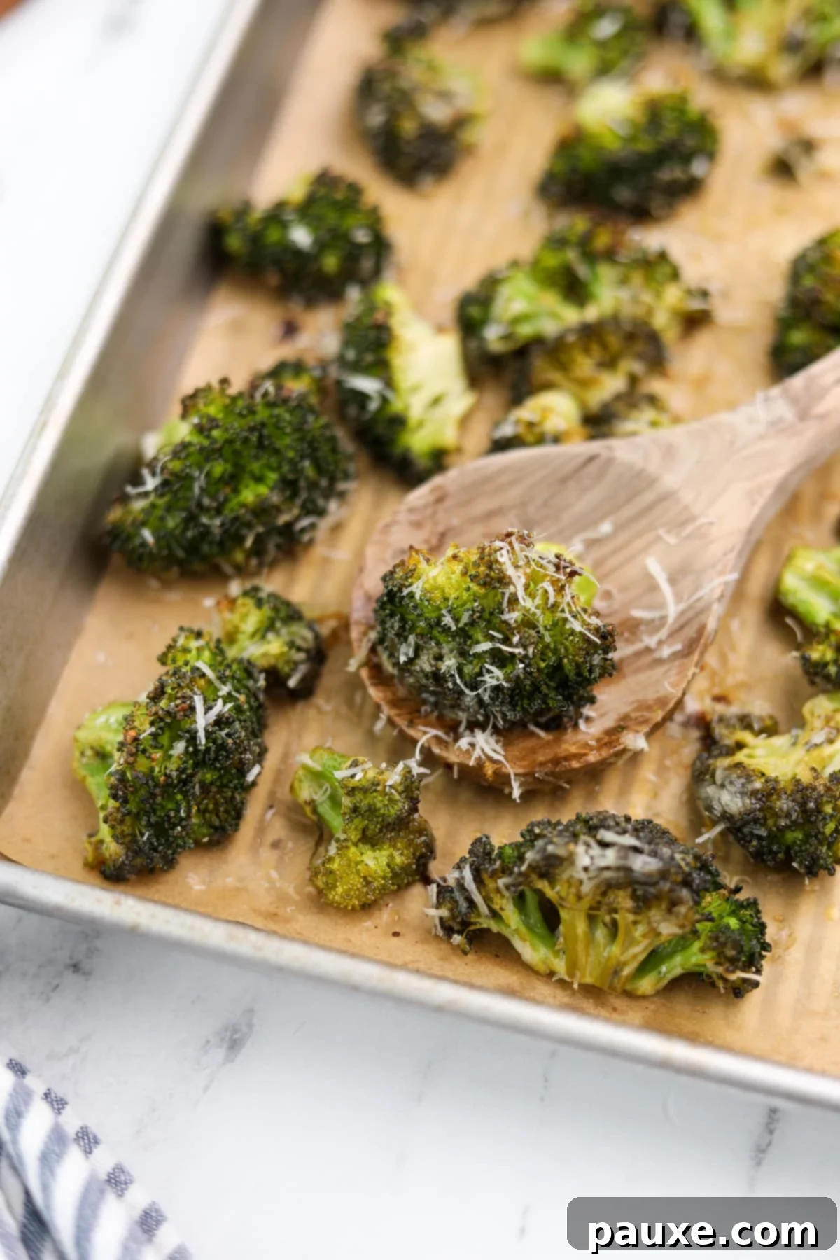Zesty Ranch Roasted Broccoli 2 A wooden spoon taking a portion of perfectly roasted ranch broccoli from a baking sheet, showcasing its golden-brown edges and vibrant green florets.